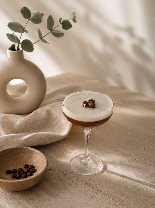 I'MI.STORE espresso martini cocktail candle in a stemmed glass with wax coffee beans on a neutral textured table.